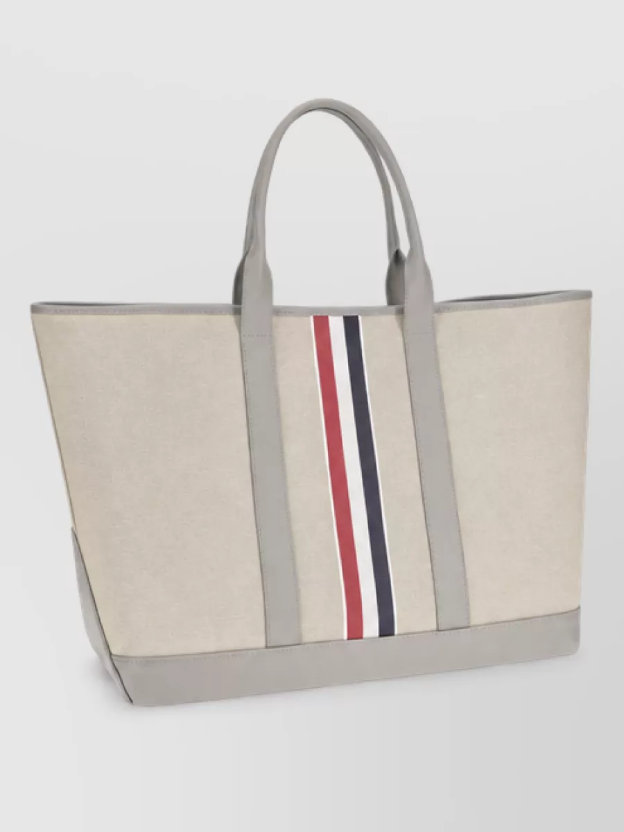 Thom Browne Fabric tote bag — The light beige Thom Browne tote with grey trim and tricolour stripe quietly repeats the house codes and palette of navy, white and soft neutrals while feeling structured enough for office-to-weekend use.