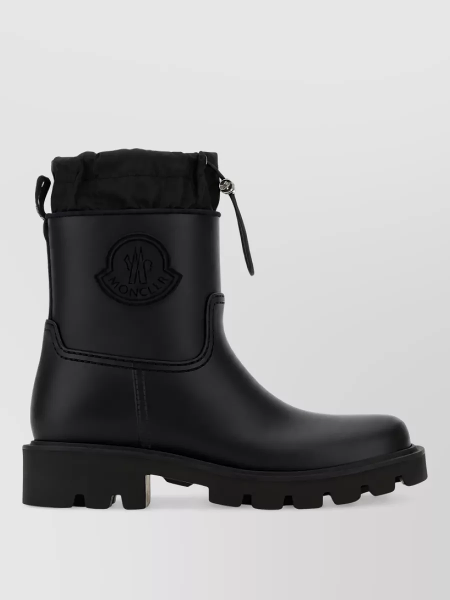Moncler Pvc ankle rain boots — The black mid-calf Moncler Genius lug-sole boots keep the line dark and streamlined, reinforcing the technical city-winter vibe and working proportionally with both the skirt and long parka.