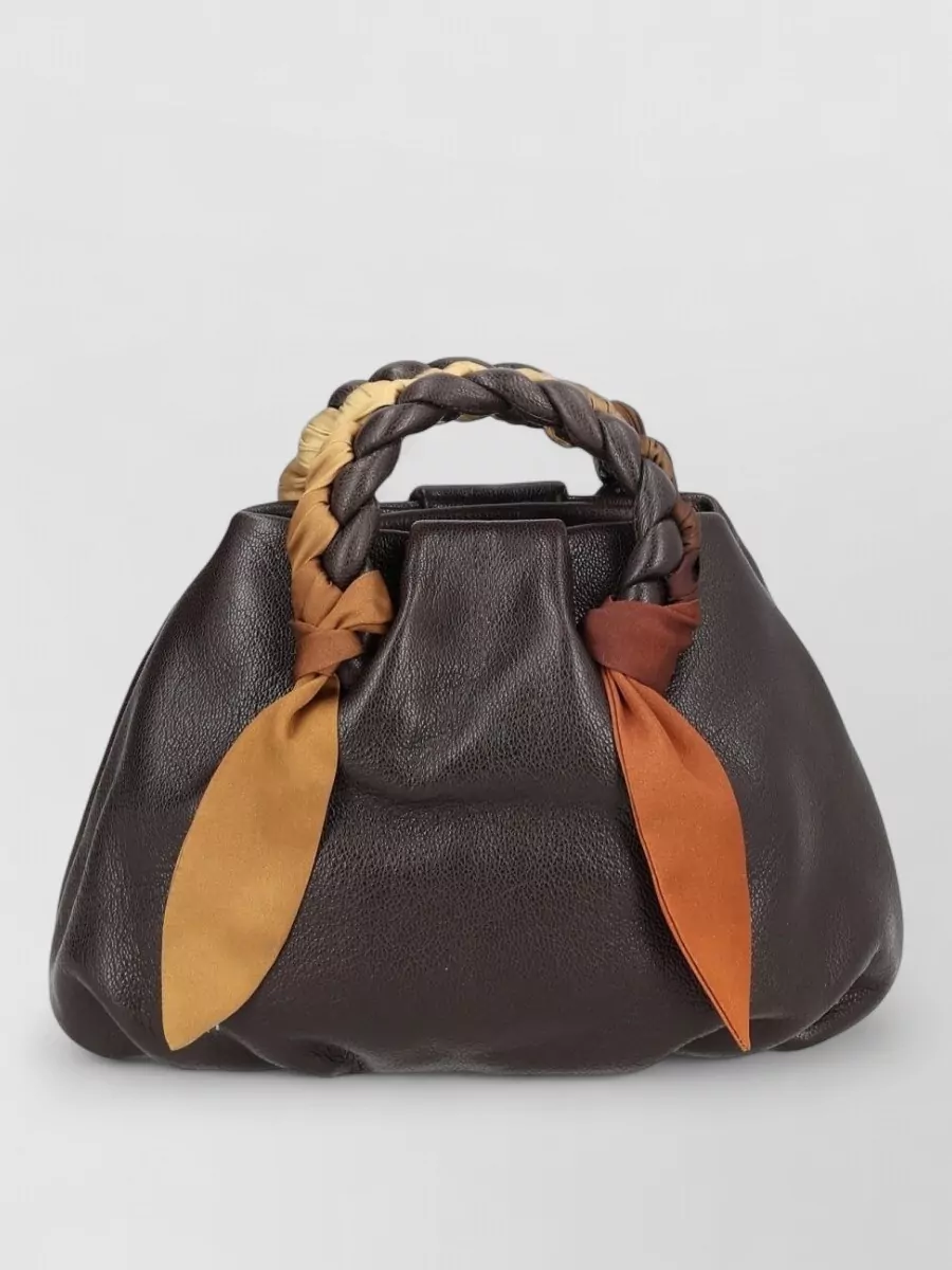 Hereu Lamb leather shoulder bag — The Hereu braided-handle bag in rich chocolate and rust adds artisanal, boho-inflected warmth and texture without disrupting the black column, while staying in the same quiet luxury tier as the boots and dress.