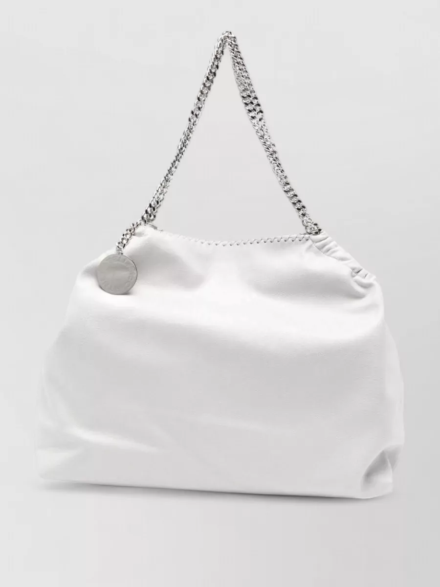 Stella Mccartney falabella drawstring shoulder bag — The soft ivory chain-trim tote echoes the silver hardware at the neckline and stays within the light neutral palette, reinforcing the quiet luxury story without adding contrast.