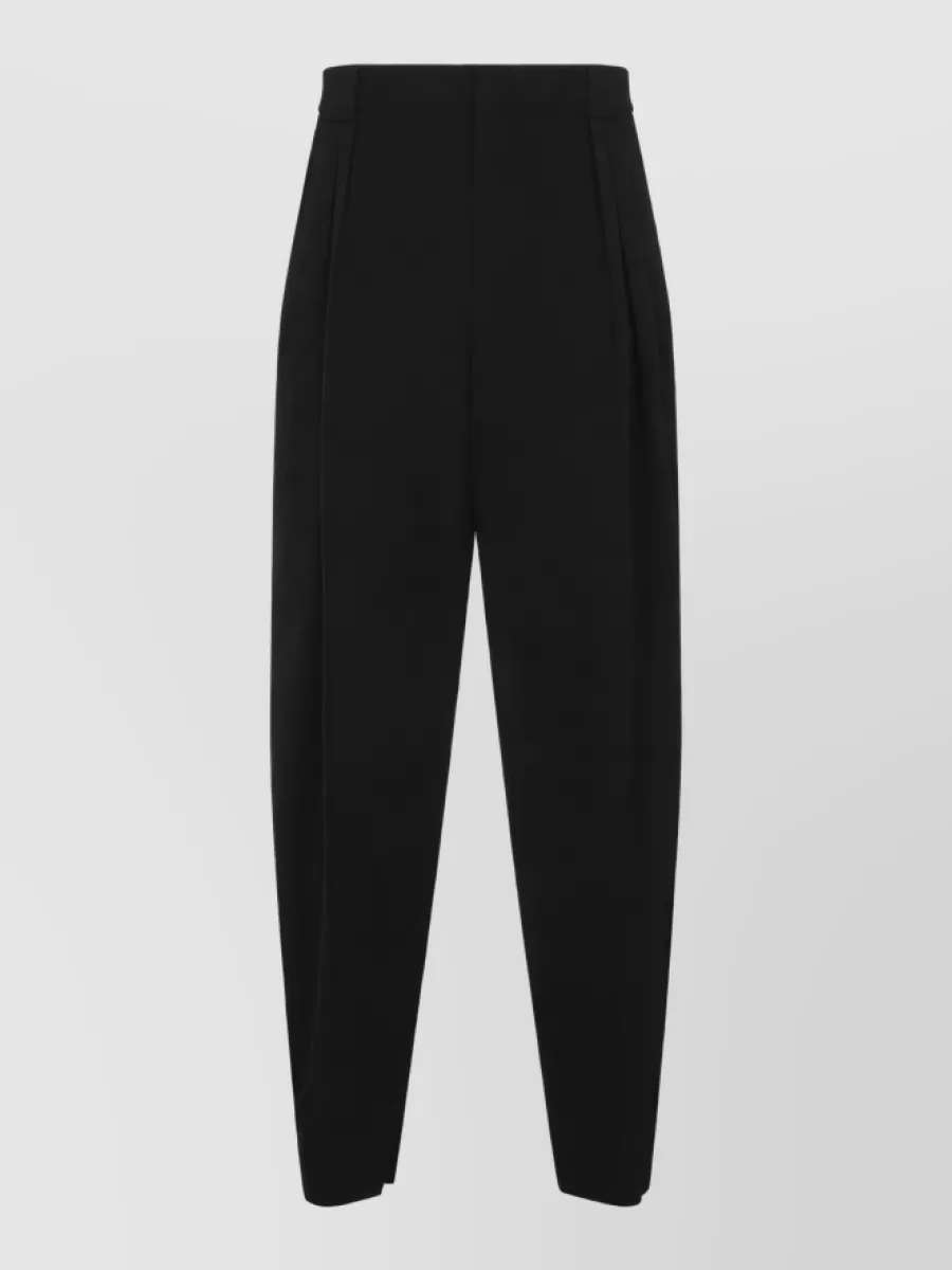 Bottega Veneta Wool high-rise pleated tapered tailored trousers — The high-rise black and charcoal pleated trouser matches the vest’s sharp minimalism, elongates the line under a cropped elasticated hem, and stays within the same quiet luxury tailoring tier.