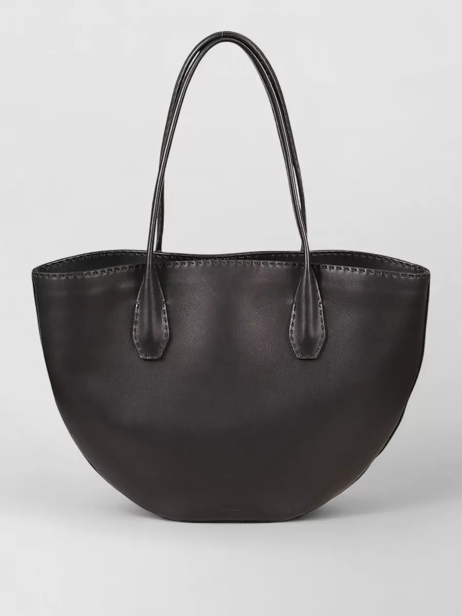 The Row Leather tote bag — The Row’s sculpted black tote matches the dress and boots tonally while adding a subtly architectural counterpoint to the soft coat, maintaining a fully elevated, logo-free narrative.