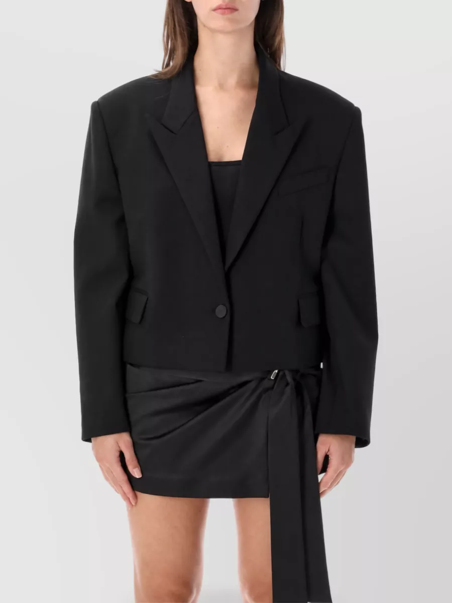 The Attico Virgin wool embroidered blazer — The cropped black Attico blazer mirrors the skirt’s sharp wrap drama, keeps the palette monochrome and formality high, and shows just enough midriff to balance the very short mini.