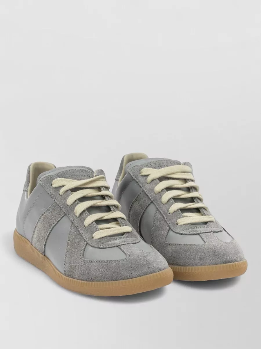 Maison Margiela Leather low-top sneakers — The iconic grey Margiela sneakers sit perfectly in the same quiet-luxury streetwear space as the tee, their gum sole and soft tones tying into the light denim and keeping the mood relaxed.