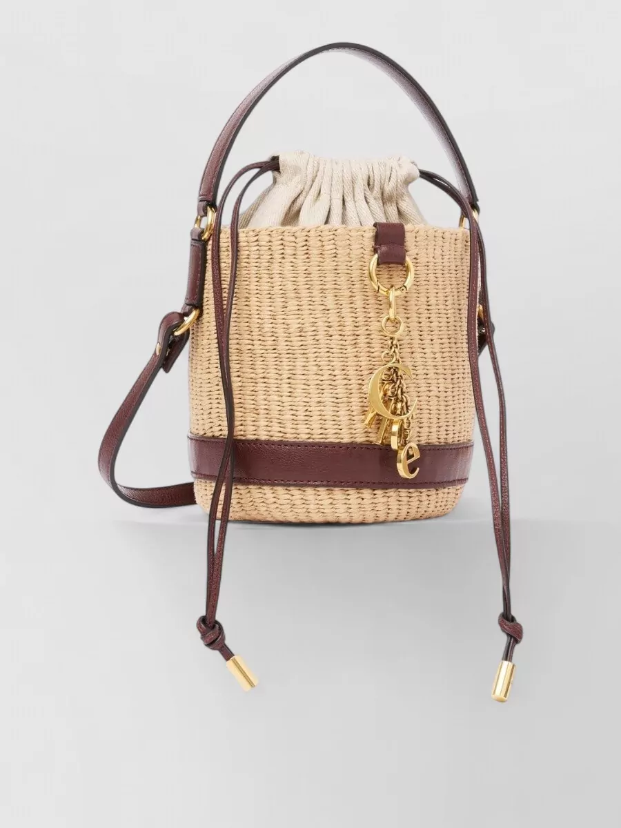 Chloé Na bucket bag — The Chloé raffia mini bucket in natural and deep brown echoes the sandal’s tortoiseshell and caramel palette while keeping the mood boho and polished without overpowering the dress.