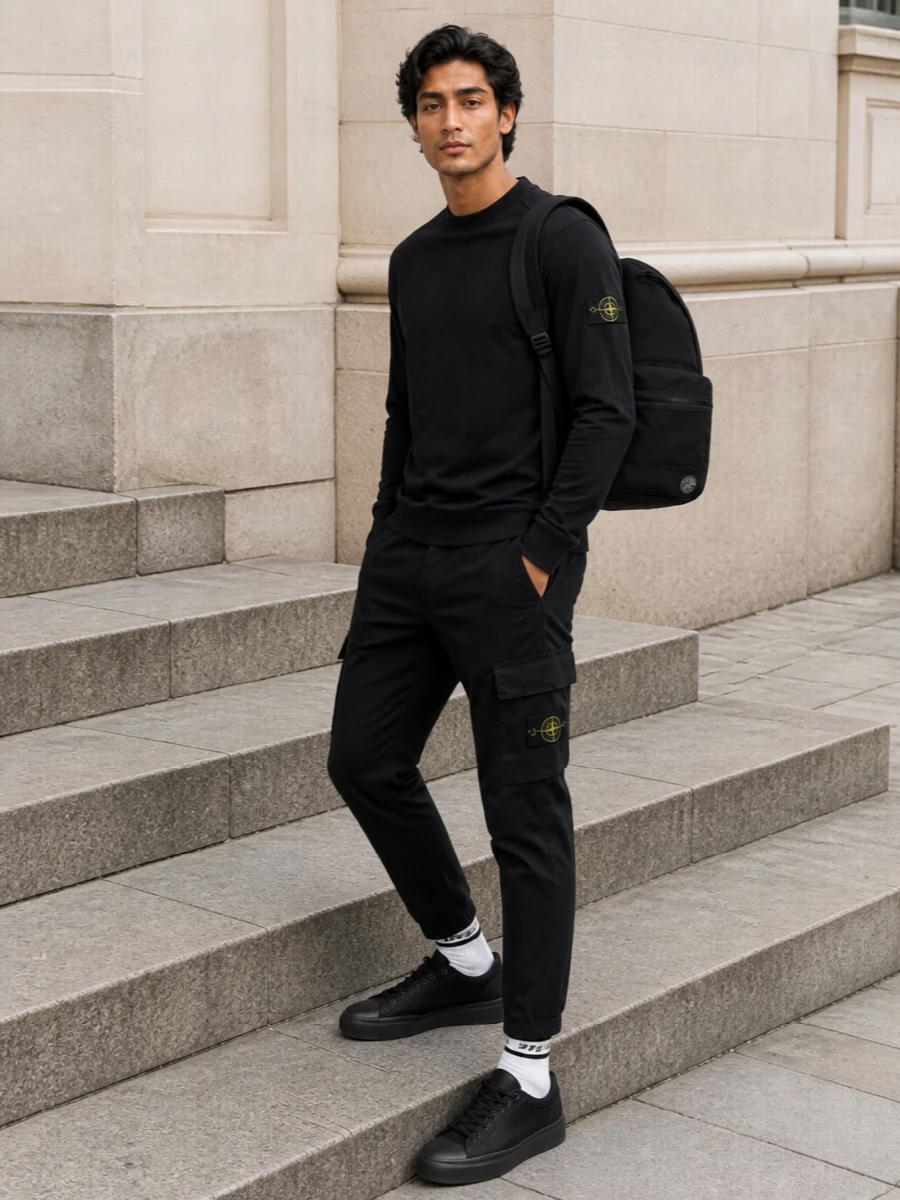 A tight Stone Island uniform built around deep black and technical texture, this pairing focuses on clean lines and logo hits rather than noise. Straight cargos keep the silhouette grounded under the structured long-sleeve, while black technical sneakers and a streamlined backpack reinforce a city-ready, sport-inflected mood. The striped socks give just enough contrast at the ankle to break the monochrome without diluting the minimal edge.