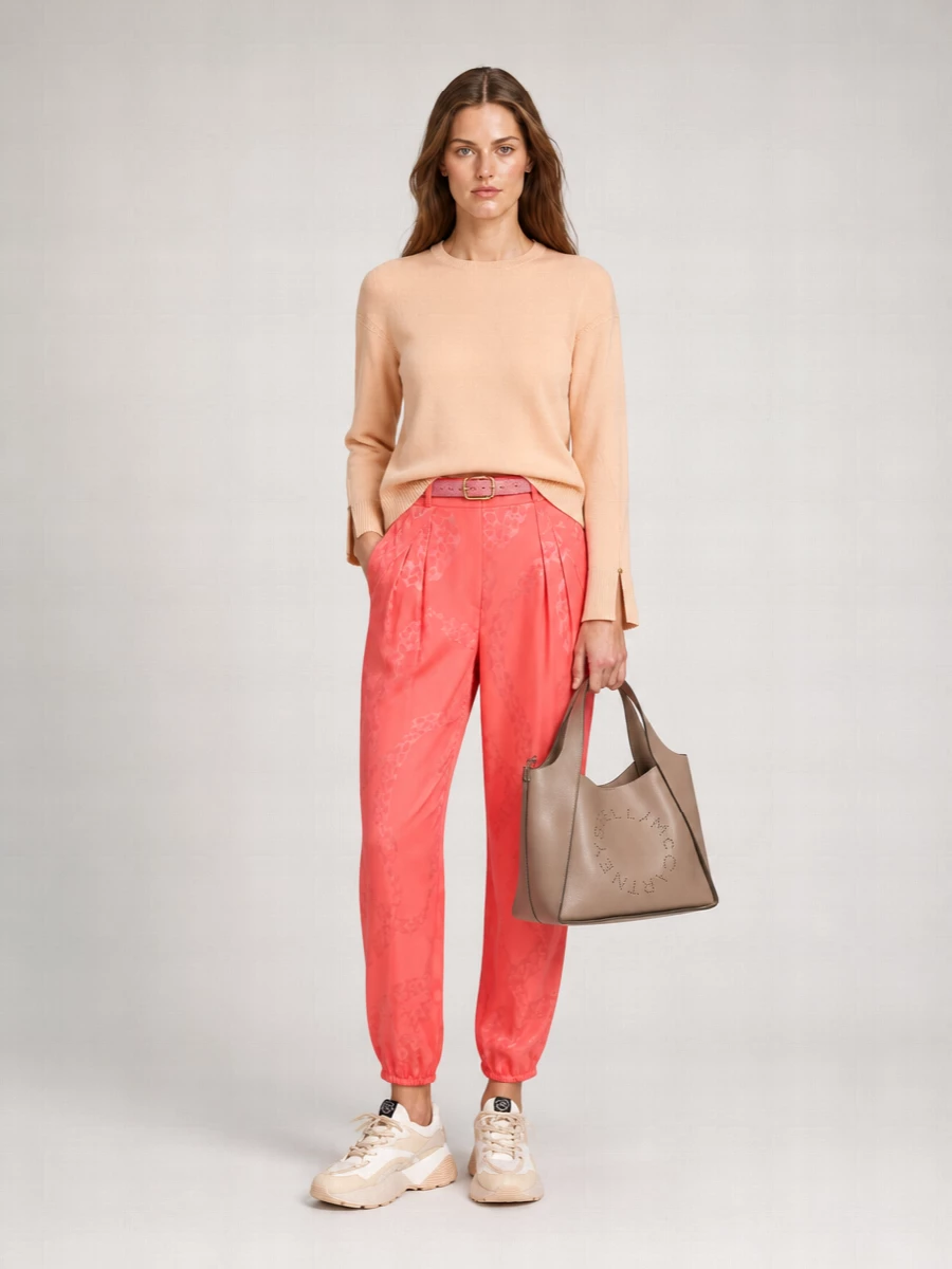 Coral tapered trousers are softened with a peach knit, creating a romantic yet clean column of warm colour. Chunky tonal sneakers keep the mood modern and relaxed, while a blush structured tote and dusty-rose belt pull the pink story together with quiet precision. It is an easy city outfit that feels tailored enough for daytime plans but still playful in palette.