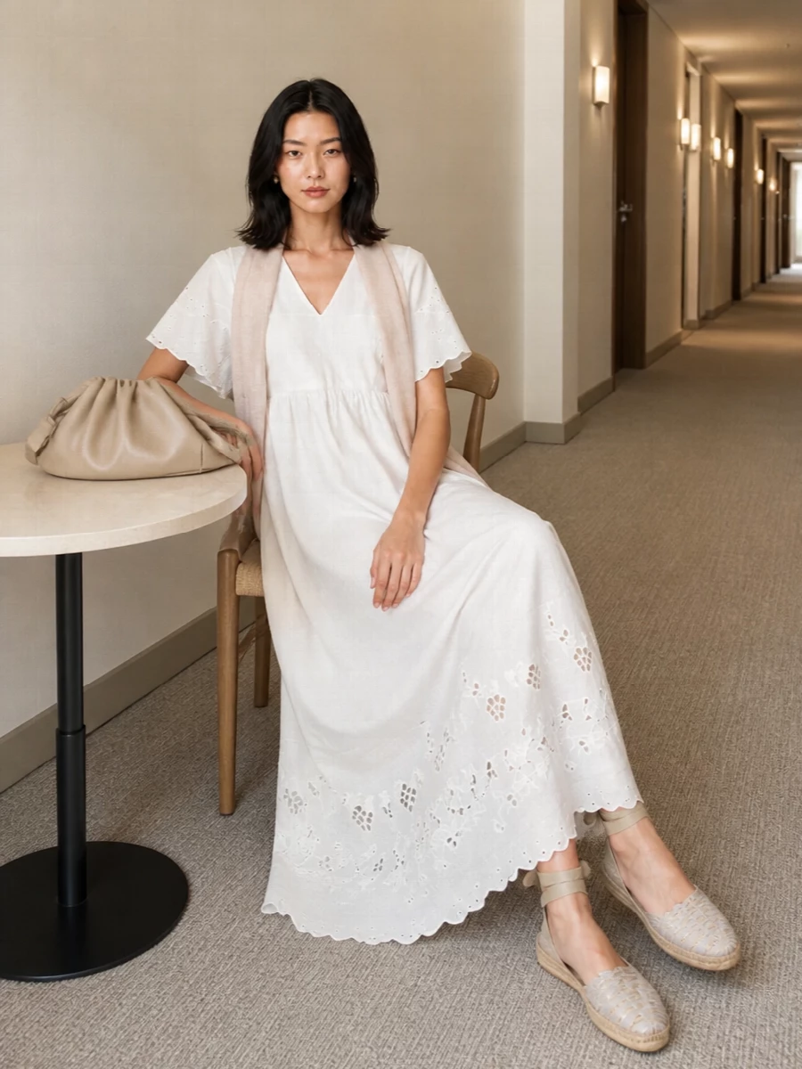 Soft white, sand and warm beige keep this maxi dress firmly in quiet summer territory, with the ankle-tie espadrilles and ruched shoulder bag adding a relaxed Mediterranean mood. Pearl studs and a gauzy blush wrap give just enough refinement for garden parties or terrace dinners while letting the broderie hem and easy A-line do the talking. The result is airy, romantic and polished without feeling dressed up for no reason.