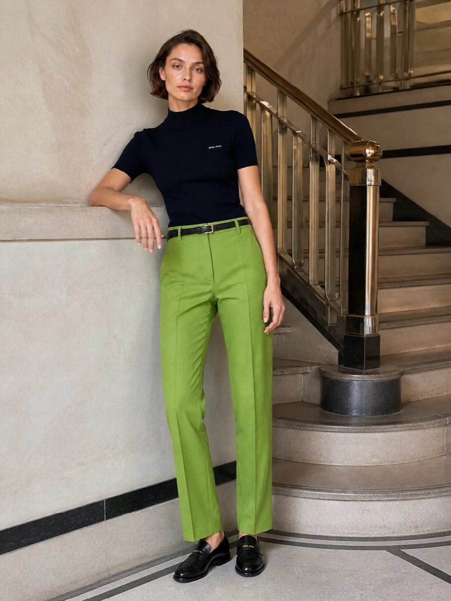 Lime tailored trousers and a navy mock-neck knit create a crisp, collegiate color story that still feels grown up. Black loafers and a compact top-handle keep everything taut at the hem and hand, so the cut of the trouser does the talking. A slim black belt finishes the waist with just enough definition for office or dinner in the city.