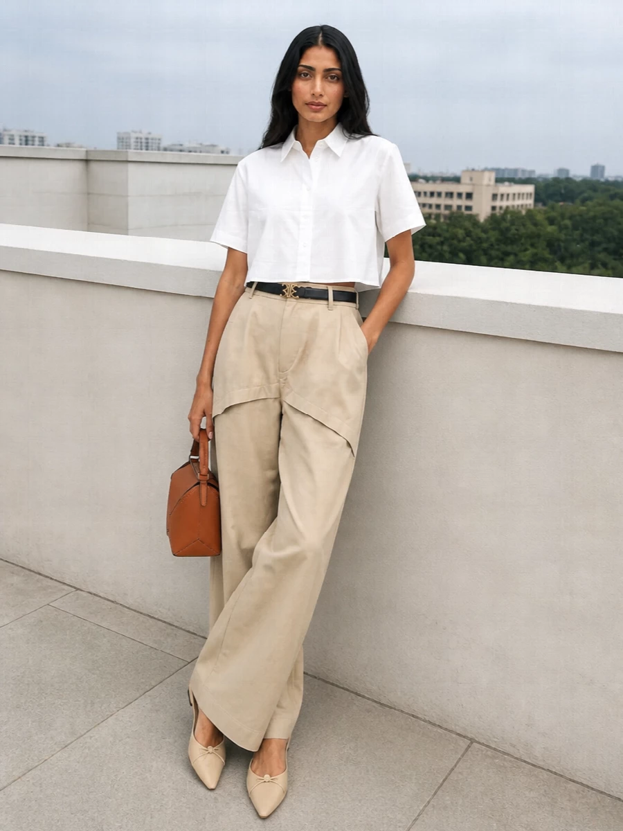 A crisp white cropped shirt is grounded by sculpted sand wide-leg trousers for a clean, elongated silhouette. Butter-soft nude flats keep the attitude relaxed yet precise, while a tan geometric shoulder bag and slim black belt add quiet structure and depth. The result is a minimalist, city-ready ensemble that moves easily from daytime meetings to low-key dinners.
