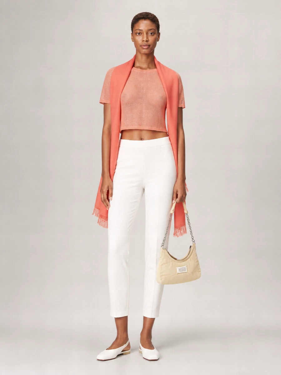 Soft white knit trousers ground the sheer coral tee in a clean, elongated line that still feels relaxed for warm days. White slingbacks and a butter-beige crescent bag keep the neutrals creamy and understated, letting the knit’s color do the quiet talking. A tonal coral wrap finishes the palette with a considered, sun-washed harmony.