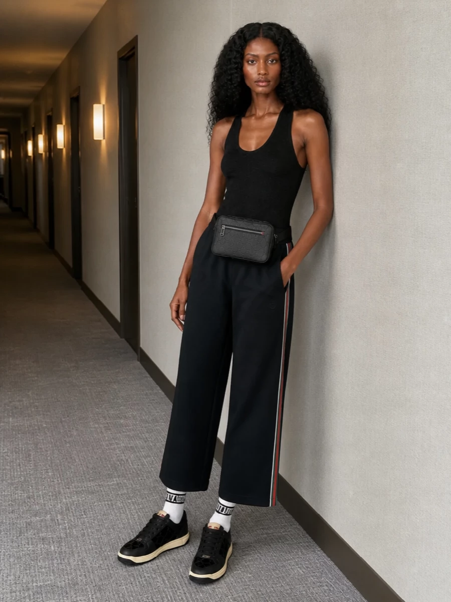 A slim black Gucci tank meets fluid black track pants for a sleek, sport-driven silhouette that feels relaxed but sharply considered. Black sneakers and a compact belt bag keep everything streamlined and practical, while graphic socks add just enough attitude. It is an easy city uniform that reads athletic, modern and quietly logoed up close.