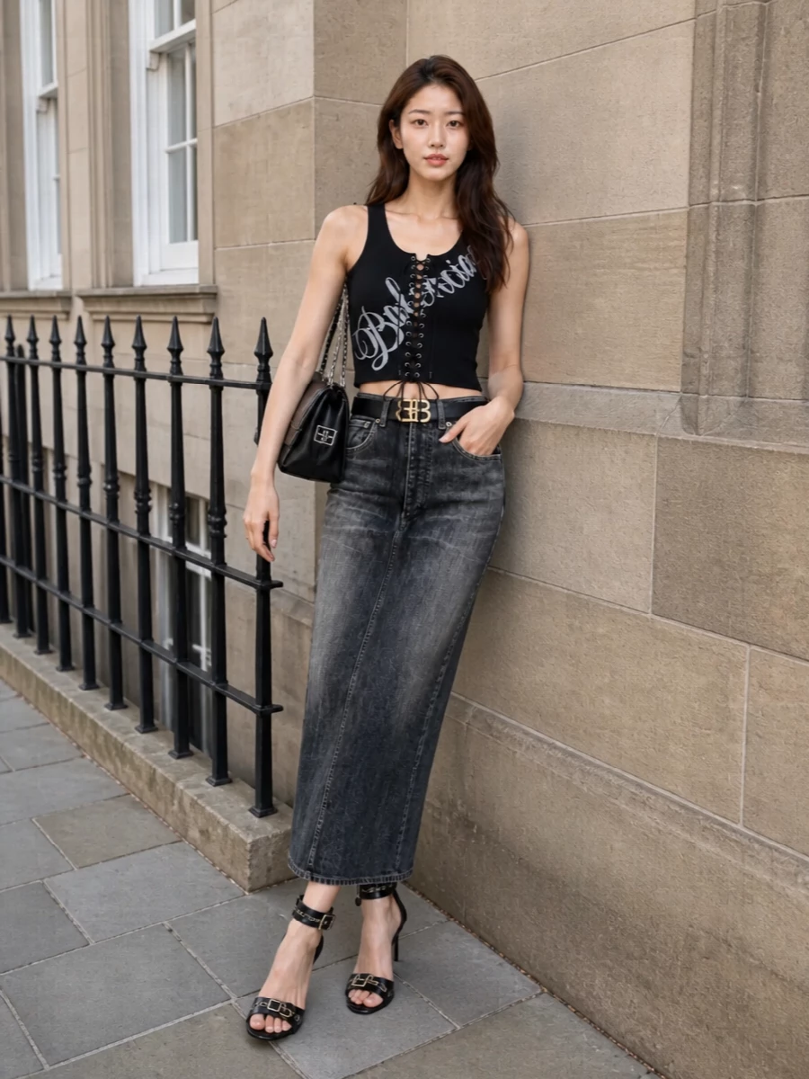 Balenciaga’s corseted tank tops a slim, vintage-faded denim midi for a long, grungy line that still reads sharply put together. High stiletto sandals and a chain-strap BB shoulder bag pull it straight into late-night city energy, while a slim logo belt quietly defines the waist. The palette stays dark and graphic so the lacing and hardware feel intentional rather than busy.