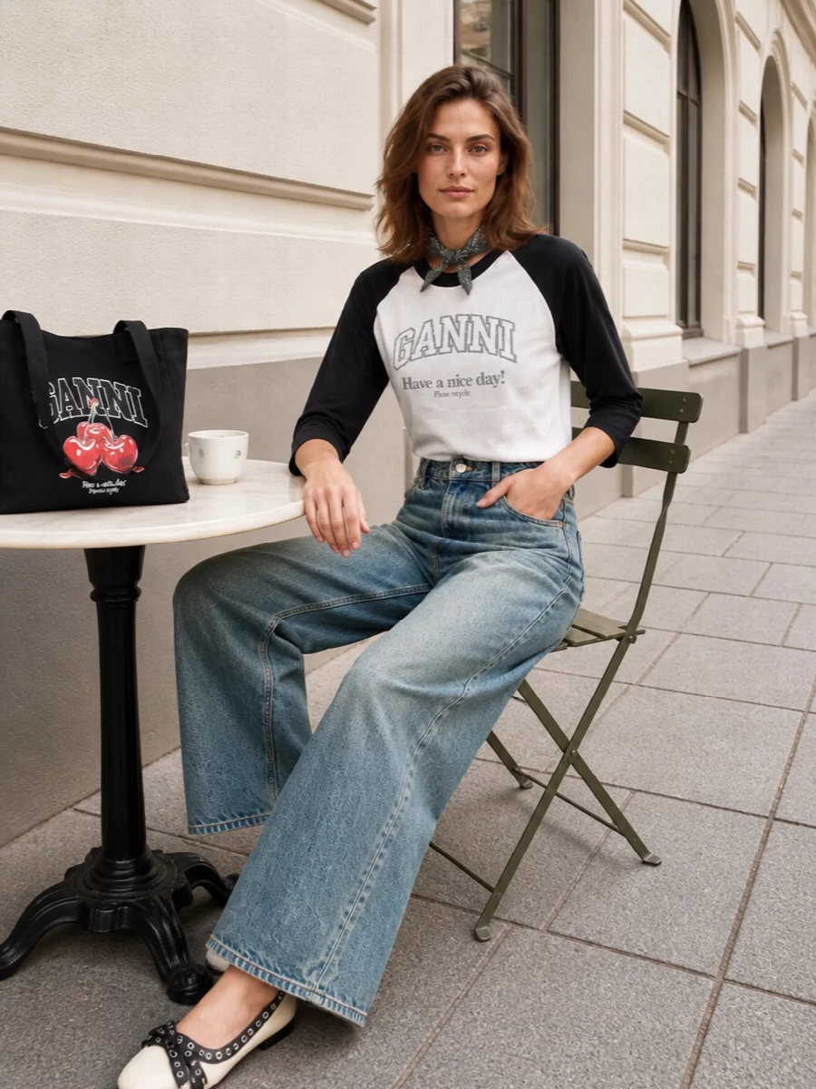 A graphic raglan tee meets high-rise wide-leg denim for a clean, borrowed-from-baseball take on city casual. Cream-and-black ballerinas and a slogan tote keep the palette tight while dialing up the playful, preppy edge. A charcoal bandana finishes it with a small, considered hit of attitude you can wear at the neck or knot to your bag.
