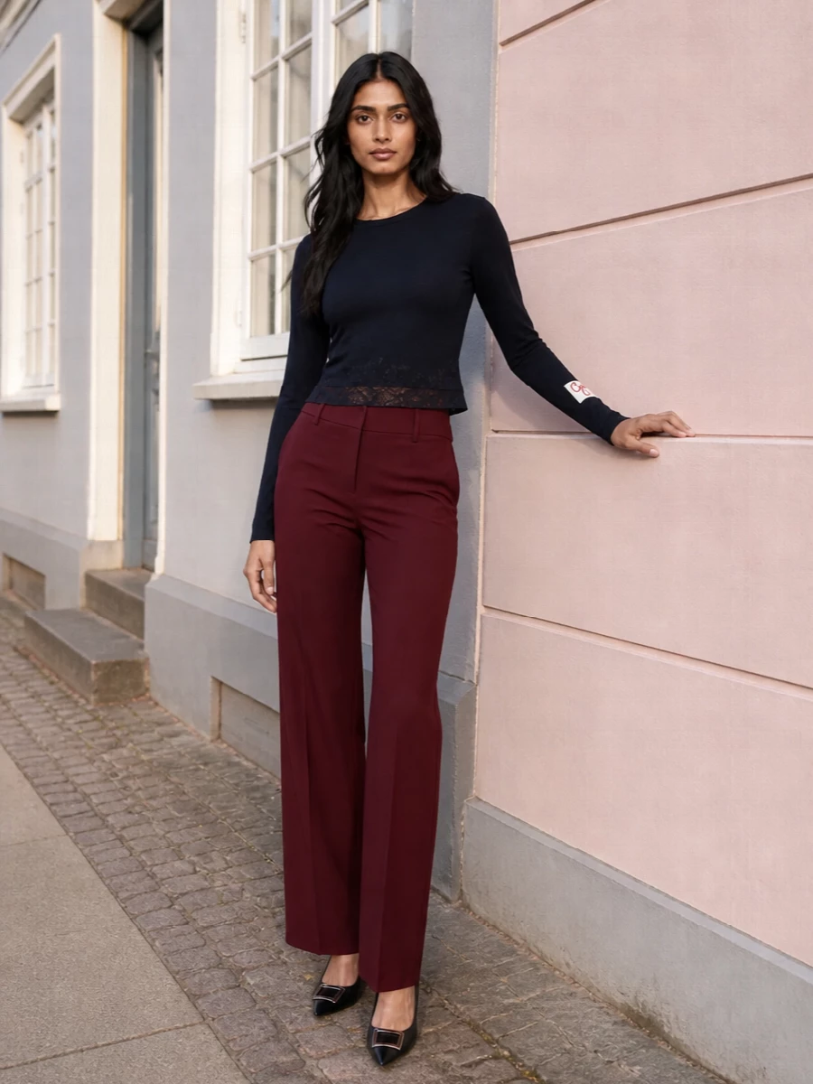 Deep burgundy tailoring meets a slim navy knit for a quietly assertive, desk-to-dinner pairing. Black pointed pumps refine the long, clean leg line, while a structured black top-handle bag keeps the mood purposeful and polished. The result is sharp, minimal and unmistakably grown up.