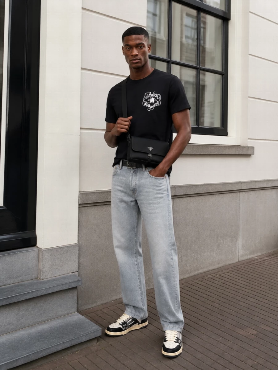 A monochrome Amiri tee sits over washed light-grey denim for a clean, low-key take on LA street energy. Cream and black sneakers keep everything graphic but not loud, while a structured Prada crossbody and precise black belt bring in a quiet, technical luxury that still feels relaxed and wearable day to night.