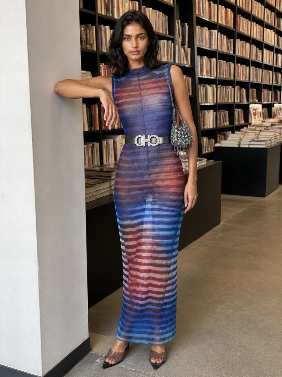 A sheer Gaultier column like this wants everything around it quiet and sharp, so the accessories stay in a smoked black and silver register. Transparent kitten mules and a crystal-buckled belt echo the mesh and stripe the line of the body, while a liquid silver fringe bag brings all the movement and light the dress is asking for. The result is lean, graphic and ready for late-night rooms where the print does all the talking and the hardware just glows around it.
