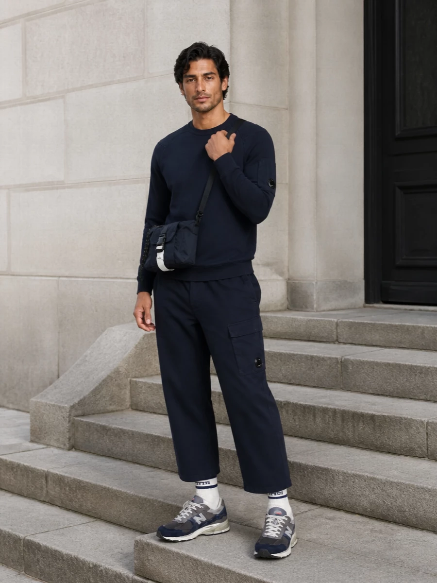 Head-to-toe navy keeps this C.P. Company outfit sharp, letting the lens hardware and technical textures do the talking. The relaxed straight-leg utility trousers balance the clean crew sweat, while the retro runners and compact crossbody lean it toward easy city movement. Off-white striped socks give just enough contrast to keep the palette from feeling flat while staying firmly in the streetwear utility universe.