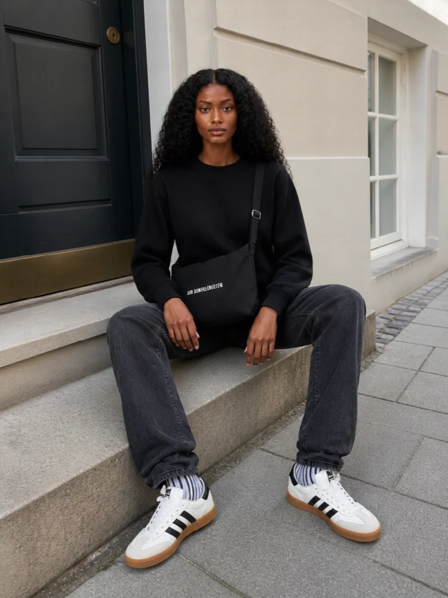 A black Frankie Shop sweatshirt and washed-black straight denim create a low-key, tonal base with just enough structure to feel intentional. White-and-black gum-sole sneakers, a softly structured logo crossbody and graphic socks pull in contrast and texture, keeping the silhouette clean, long and quietly urban.