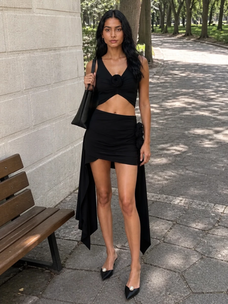 A tight black-on-black story keeps the rosette details feeling graphic rather than girlish, with the high-waisted mini framing the cropped top into a clean hourglass. The kitten-heel mules and petite structured tote refine it just enough for warm-night parties where you want impact but still be able to move. It is sultry, sculpted and very Y2K in attitude, without a single element shouting over the others.