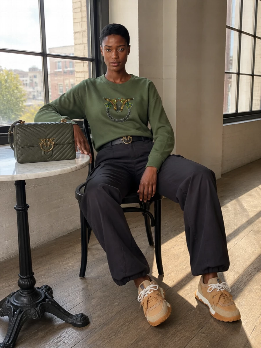 Olive sparkle and deep charcoal cargoes keep this Pinko set firmly in streetwear territory, with the jeweled crest playing off clean utility lines. Chunky camel sneakers and a quilted olive shoulder bag warm up the muted base, so the outfit feels styled, not slouchy. A slim gold-buckle belt finishes it with just enough structure to move from lazy brunch to city errands without a change.