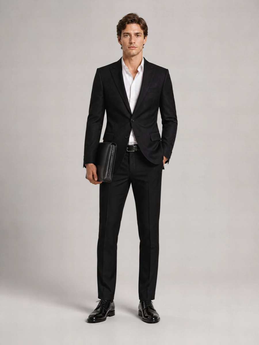 Dolce&Gabbana’s tonal-logo blazer sits over slim black tailoring for a precise, Italian evening statement that reads confident up close and impeccably restrained at a distance. High-shine derbies, a discreet leather belt and a structured pouch keep the focus on cut, texture and posture rather than branding. It is the kind of all-black suiting that feels right for everything from a formal dinner to a late-night event in the city.