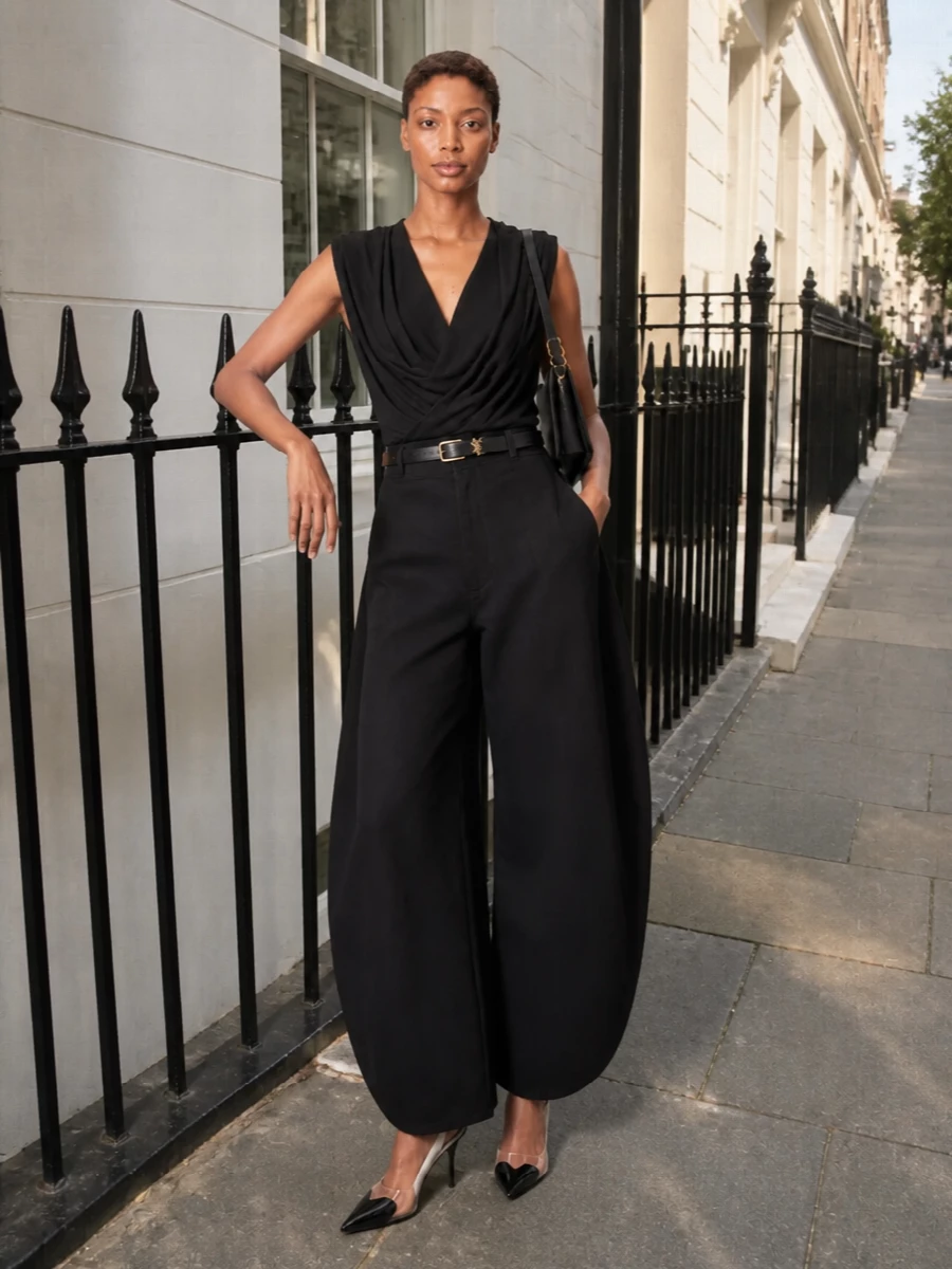 Alaïa’s draped black jersey top meets sculptural high-waisted wide-leg trousers for a graphic, all-black column that reads polished and sensual. Knife-point slingbacks and a slim, minimal belt keep the proportions razor-clean, while a structured shoulder bag adds just enough gold detail for evening without disturbing the quiet architecture.