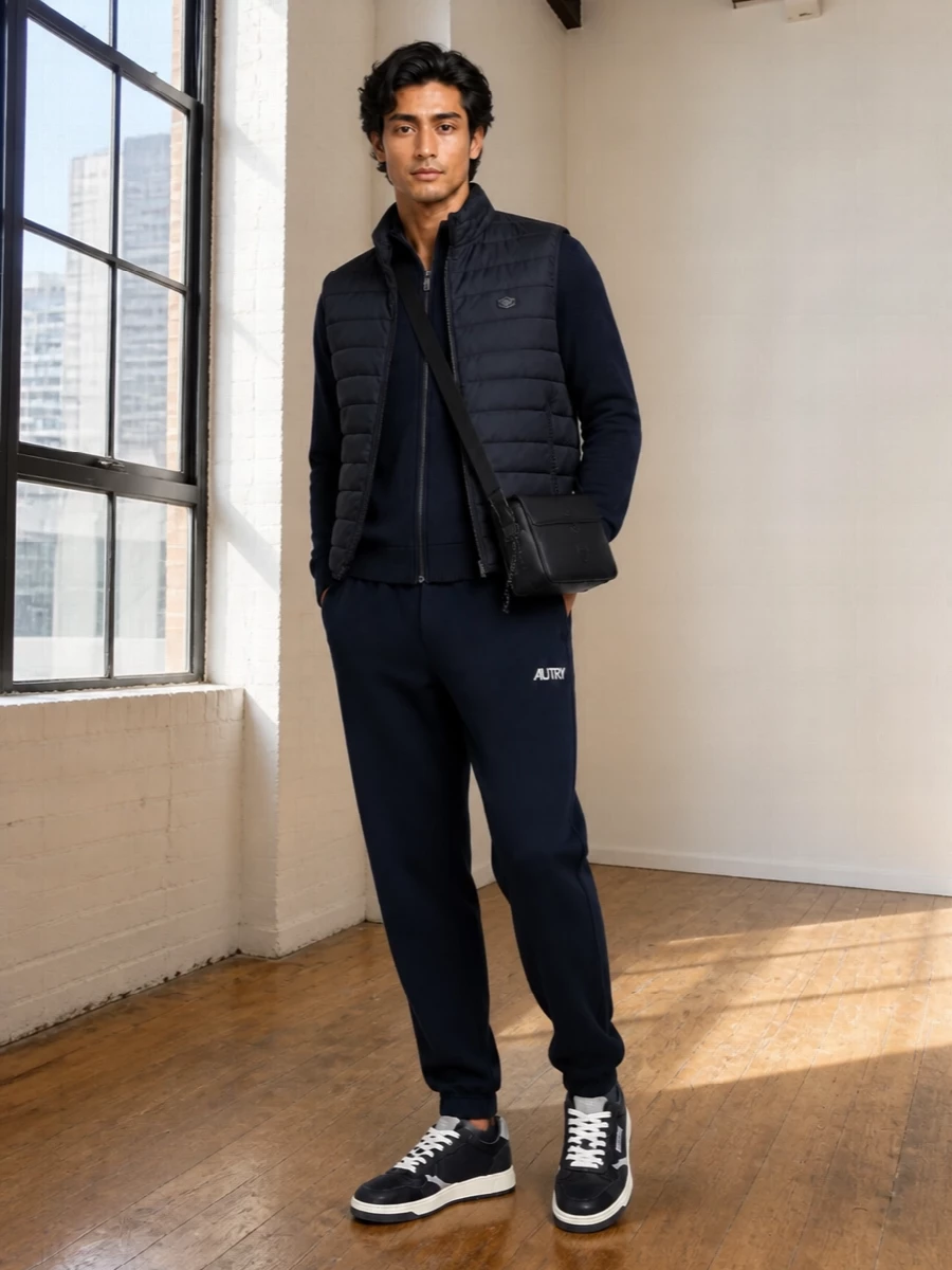 Emporio Armani’s padded gilet sits over a tonal navy knit and jogger combination for a quiet, sport-driven city uniform. Autry sneakers and a compact Moncler crossbody keep the palette dark and cohesive, turning this into an easy airport-to-weekend outfit that still feels considered.