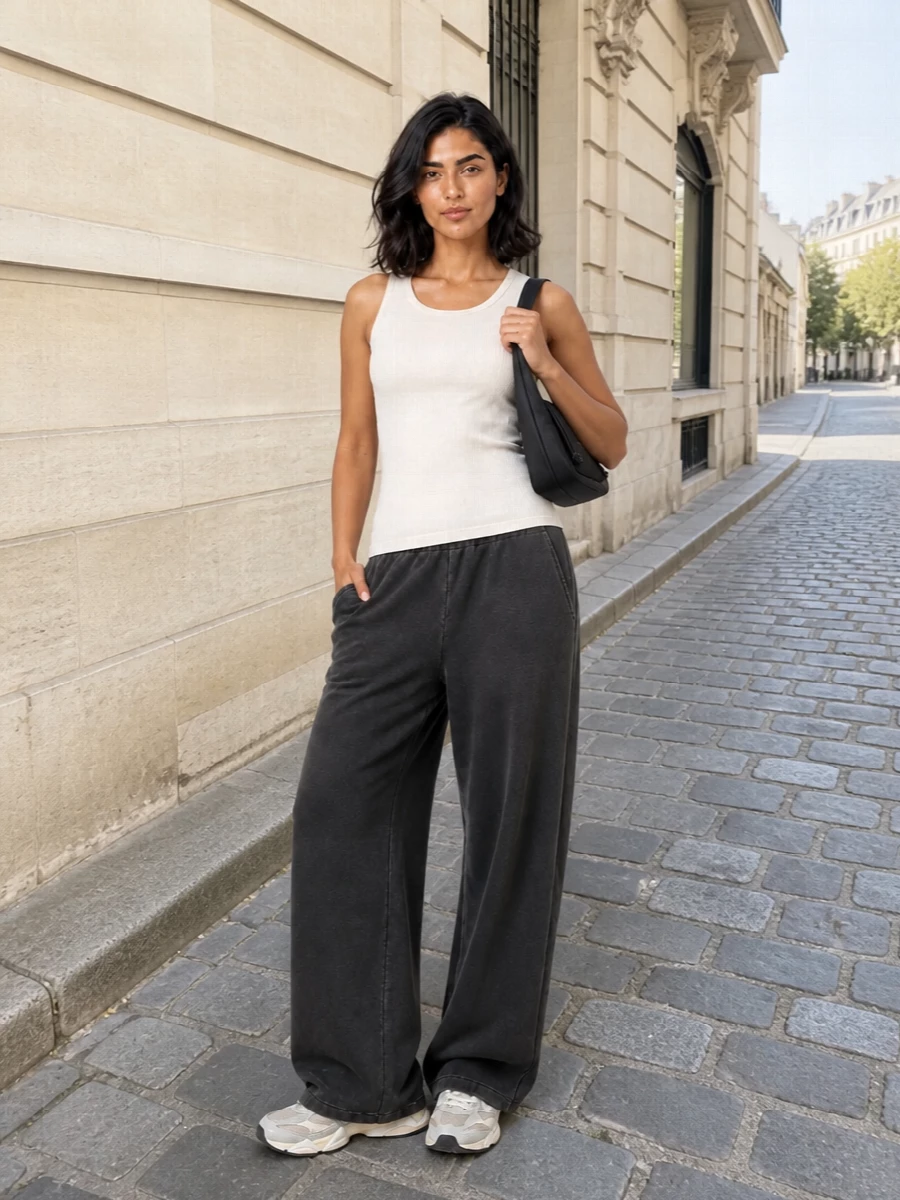 Washed charcoal wide legs and a soft ivory ribbed tank keep the outfit calm and streamlined, all about relaxed volume on the bottom and clean lines up top. Neutral grey-beige runners echo the trouser tone while adding a cushioned, fashion-aware base, and the compact black shoulder bag sharpens everything just enough for the city. It is an easy off-duty uniform that moves from couch to coffee run with a single change of accessories.