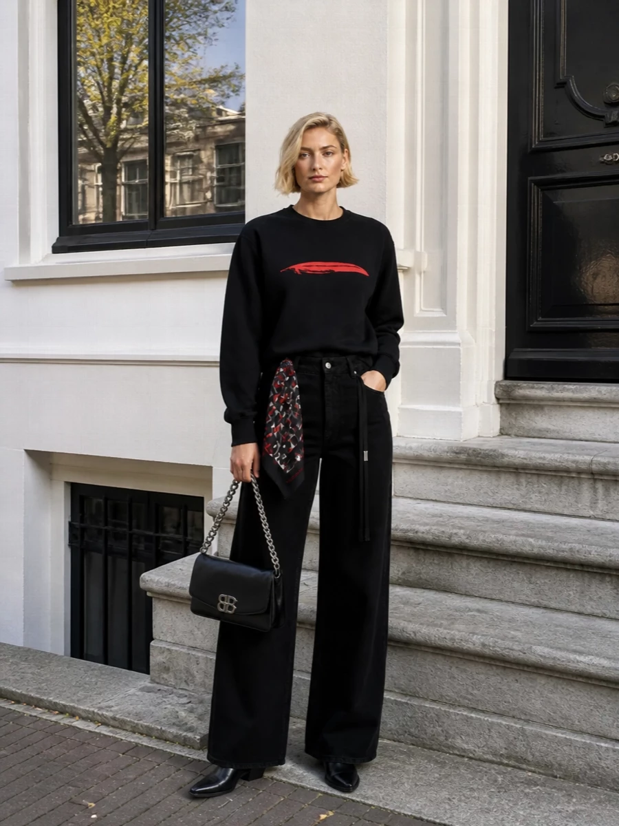 A stark black base lets the red feather do the talking, anchored by fluid high waist tailoring that keeps the mood relaxed but precise. Pointed loafers and a sharp chain strap bag bring just enough structure, while the graphic silk scarf picks up the crimson in a way that feels intentional rather than matched. It is a city ready uniform for gallery days that stretch into late dinners, dark and refined without trying too hard.