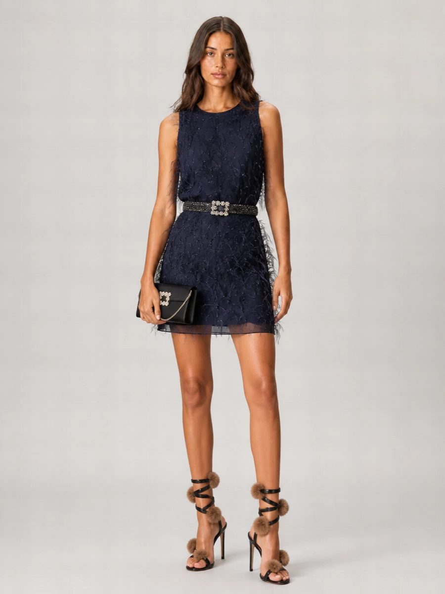 A navy feathered Pinko twinset becomes a deliberate evening statement when cinched with a crystal belt and grounded by black crystal-swirled stilettos. The palette stays inky and metallic, so all that texture reads polished, not costume. A sleek black crystal-buckle mini bag quietly finishes the party-ready ensemble without competing for attention.