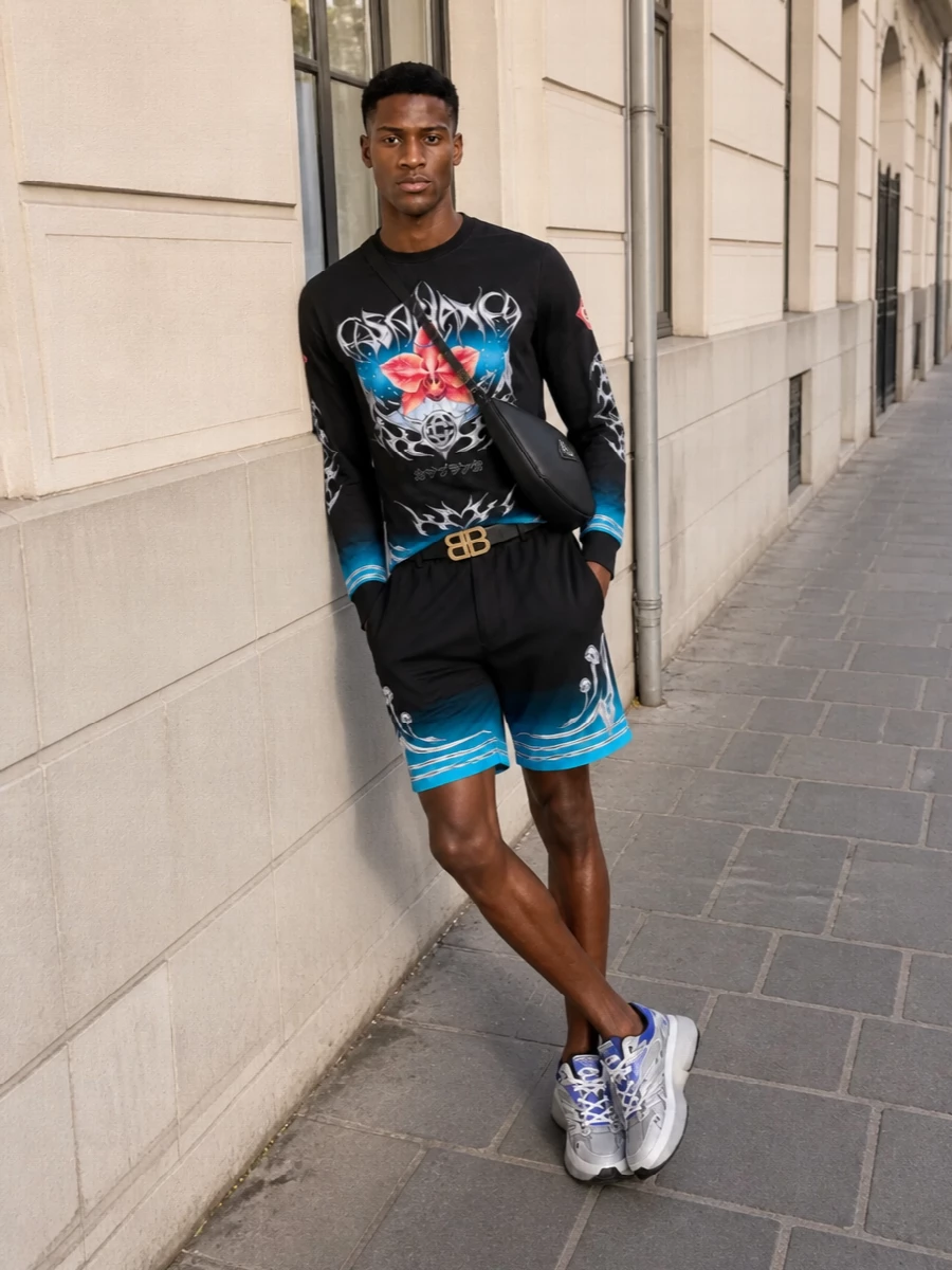 This look leans into Casablanca’s hyper-graphic energy by pairing the orchid long-sleeve with ombré mushroom shorts that echo its black and electric blue palette. Futuristic Valentino runners in ice grey and cobalt keep the silhouette sporty and directional, while a sleek black Prada crossbody and a sharp Balenciaga belt pull everything back into a focused, high-lux streetwear statement. It’s club-ready, bold and cohesive, with the tee and footwear doing the talking while the accessories stay confidently understated.