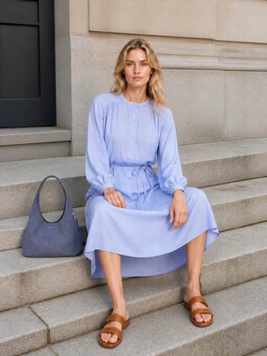 The cornflower shirt dress and slate-blue hobo bag create a calm, tonal story that feels precise but unfussy for warm days. Tan leather sandals bring a gentle contrast that keeps the palette grounded and versatile from city errands to low-key lunches. Choosing the dress route rather than separates keeps the silhouette long and simple, which suits the curved hobo’s softness and the bag’s quietly polished attitude.