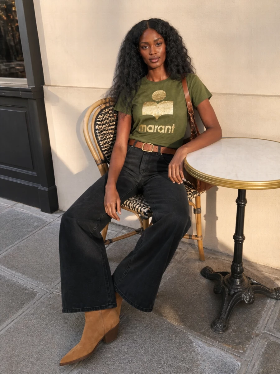 Olive and washed black set an easy base here, with the wide-leg denim giving the logo tee a long, relaxed line. Tan suede boots and a cognac saddle bag bring in that soft Western touch, keeping the mood casual but considered. A simple tan belt at the waist pulls the proportions together so the volume reads intentional, not oversized.