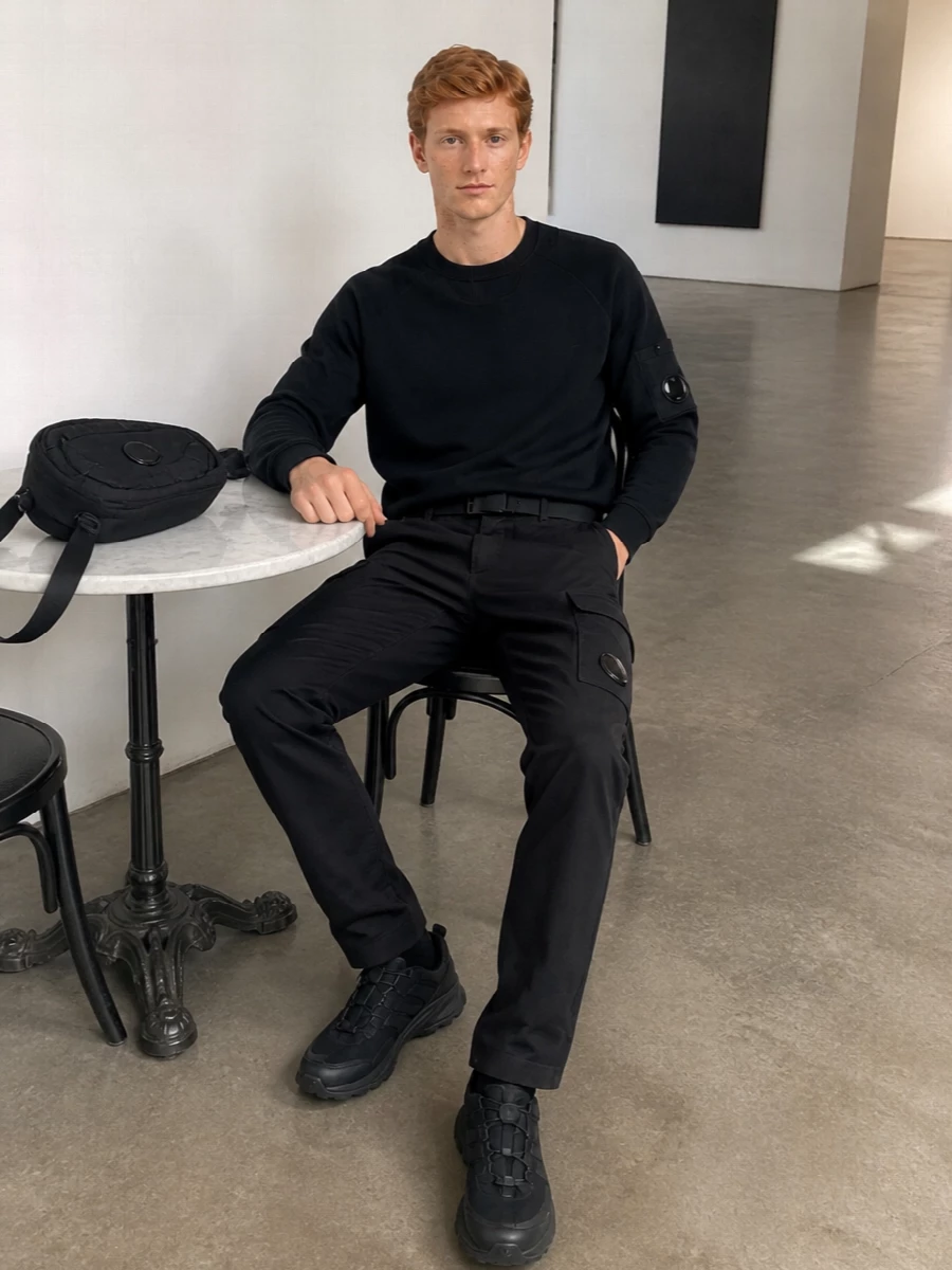Head-to-toe monochrome keeps this C.P. Company cargo pairing razor sharp, with the black crew sweatshirt echoing the same lens-driven utility as the trousers. Chunky black trail sneakers and a compact crossbody stay in the tech streetwear lane, giving you a city-ready uniform that feels modern, practical and quietly assertive. The low-key Y-3 belt pulls it together without distracting from the clean lines and hardware details.