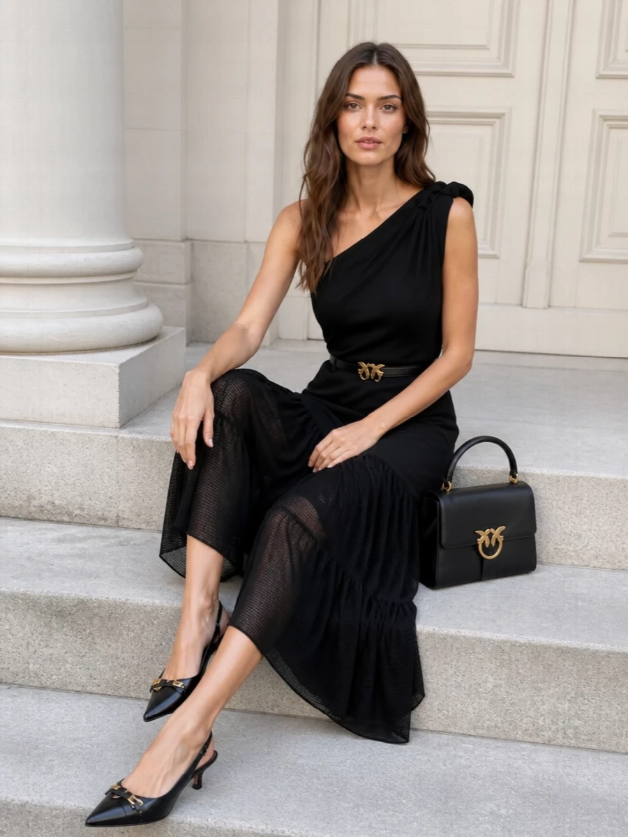 An all-black Pinko ensemble keeps the focus on line and texture, from the smocked waist and sheer tiers to the sculpted one-shoulder neckline. Gold hardware at the waist, bag and kitten-heel slingbacks adds just enough glow for warm evenings while preserving a clean, romantic silhouette. The result is quietly dramatic and easy to wear for dinners, rooftops or summer parties where you want presence without excess color.