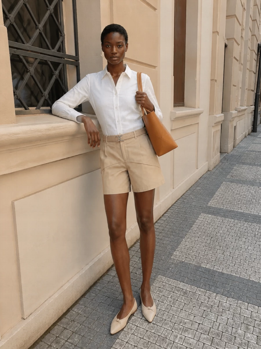 A sand-and-cream palette keeps this pairing of tailored shorts and crisp shirt calm, precise and easy for city heat. Soft pointed flats and a structured caramel tote stay within the same warm neutral story, so the proportions and details do the talking. A suede belt lightly defines the waist, keeping the silhouette clean rather than fussy.