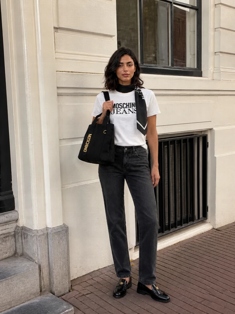 A crisp Moschino logo tee meets washed charcoal straight-leg denim for a clean, city-ready base that feels relaxed but thought through. Glossy black Moschino loafers sharpen the mood just enough, while the compact black logo tote keeps the branding tight and the proportions tidy. The McQueen scarf slips in as a monochrome accent, adding a graphic finish without overwhelming the easy street-preppy energy.