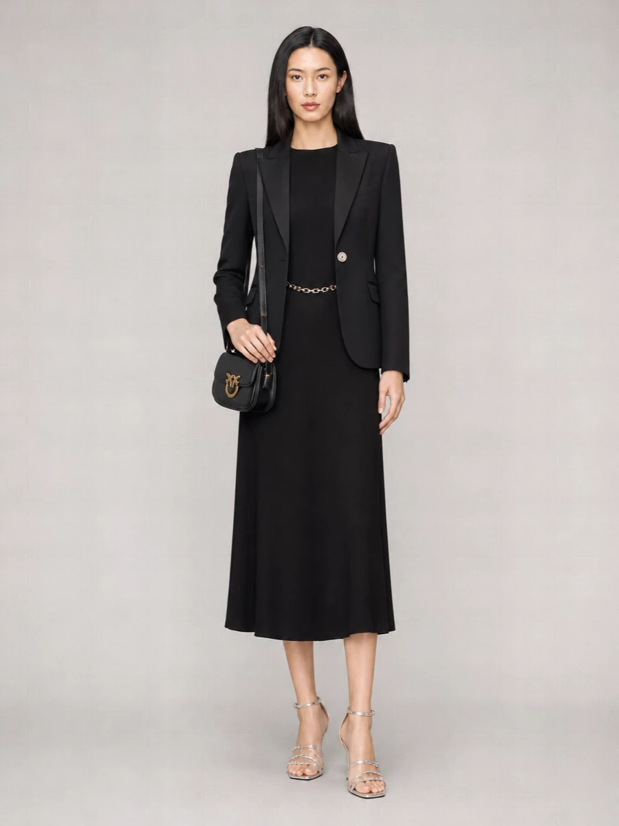 I am anchoring this around the DRESS rather than top and trouser, because the black chain-detail midi gives a single, uninterrupted column that lets the Pinko blazer read as precise outerwear instead of competing tailoring. Together they create a sharp, quietly sensual black-on-black ensemble, with the metallic chain, silver-tone button and strappy sandals providing just enough light. The compact Love Birds bag finishes it with a subtle signature touch that keeps everything in the same luxury language without tipping into fuss.