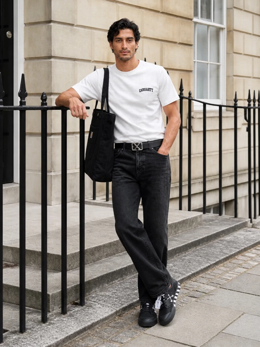 Soft white Carhartt jersey sits against washed black denim for a clean, grounded street feel. The straight-leg silhouette and monochrome sneakers keep everything relaxed yet intentional, while the graphic belt and tote add just enough attitude. It is an easy uniform for city days that leans into workwear without feeling heavy.