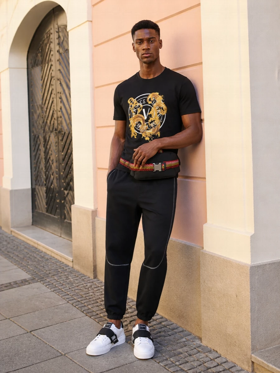 A black and gold Versace graphic tee sits over tapered black track pants for a clean, sport-leaning street uniform. The monochrome Balmain sneakers keep it sharp without overcomplicating the palette, and the Lanvin belt bag adds a practical hit of branded hardware that feels ready for the city. It is high-energy but easy to live in, perfect for days that move from errands to late-night meetups.