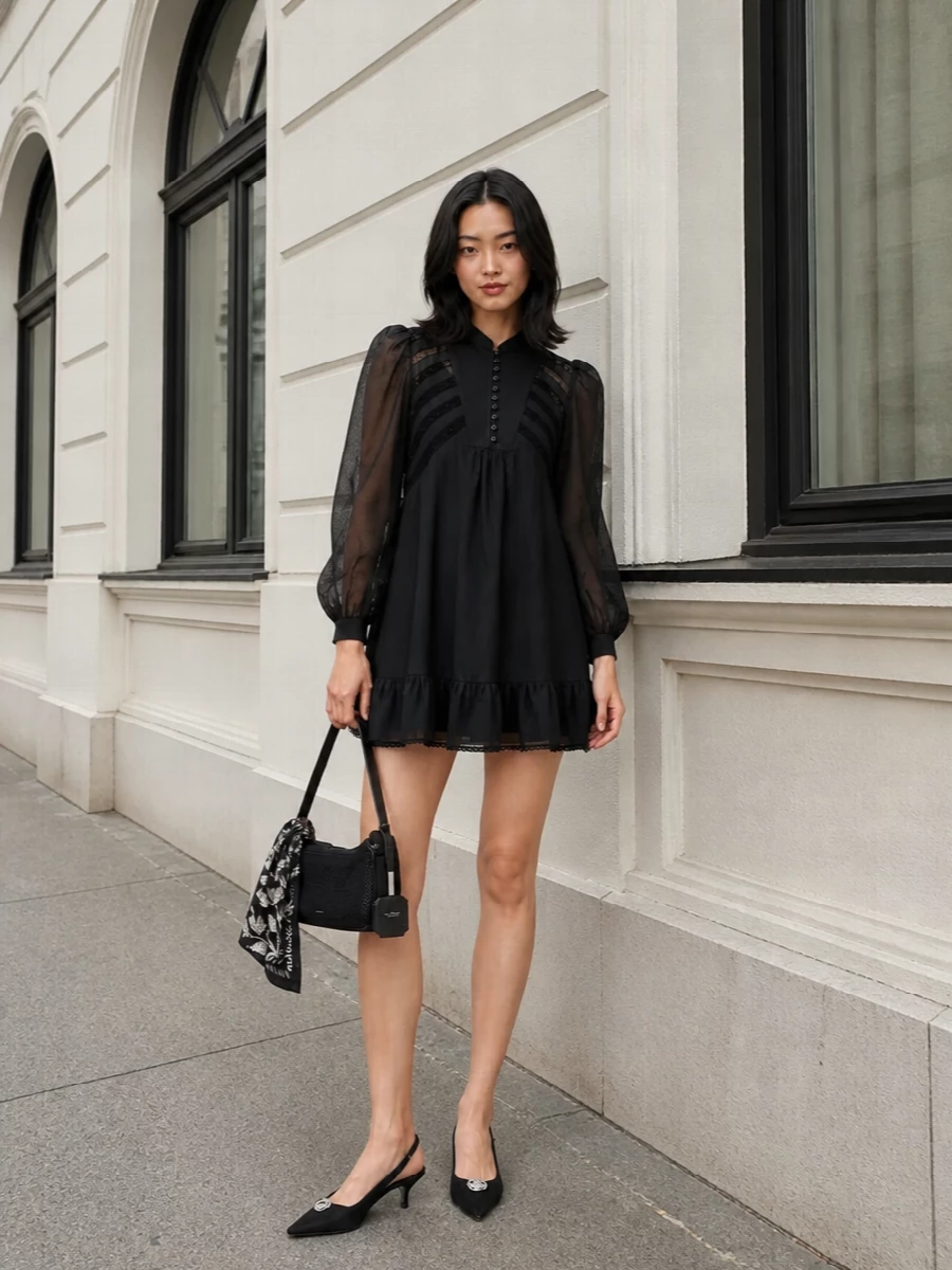 A romantic black mini meets sharp, low-key glamour, grounded by a pointed kitten slingback and a compact baguette in matching inky tones. The proportions stay light around the hem and wrists, so the outfit feels airy and suited to warm-night cocktails. A floral scarf introduces a whisper of pattern that echoes the dress’s lace without breaking the dark, quietly luxurious palette.
