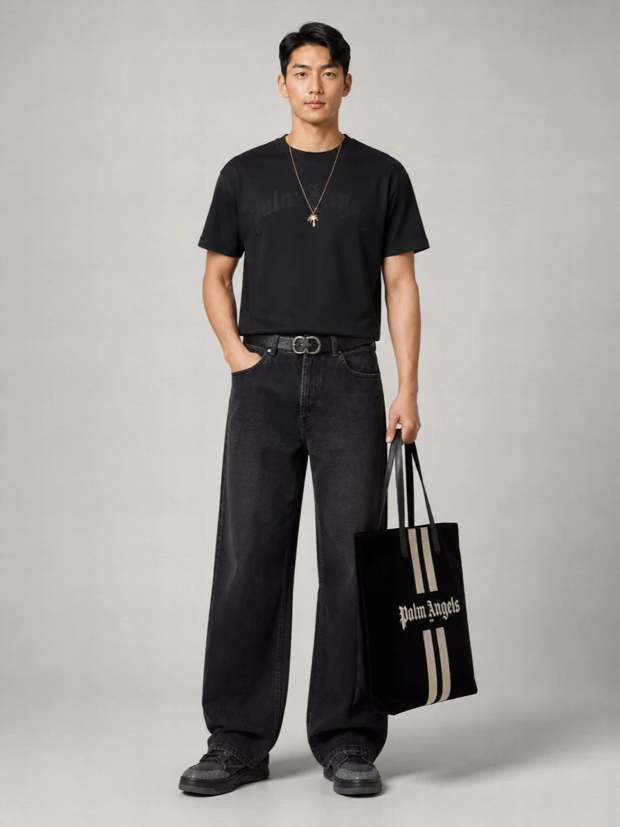 Washed-black Palm Angels on top and wide-leg charcoal denim on the bottom keep this all about low-key attitude, not loud logos. A tonal black and grey sneaker and velvet tote stay within the same muted spectrum, while a clean black belt subtly defines the waist so the wide leg reads intentional rather than sloppy. It is relaxed, straight-up streetwear that still feels considered from head to toe.