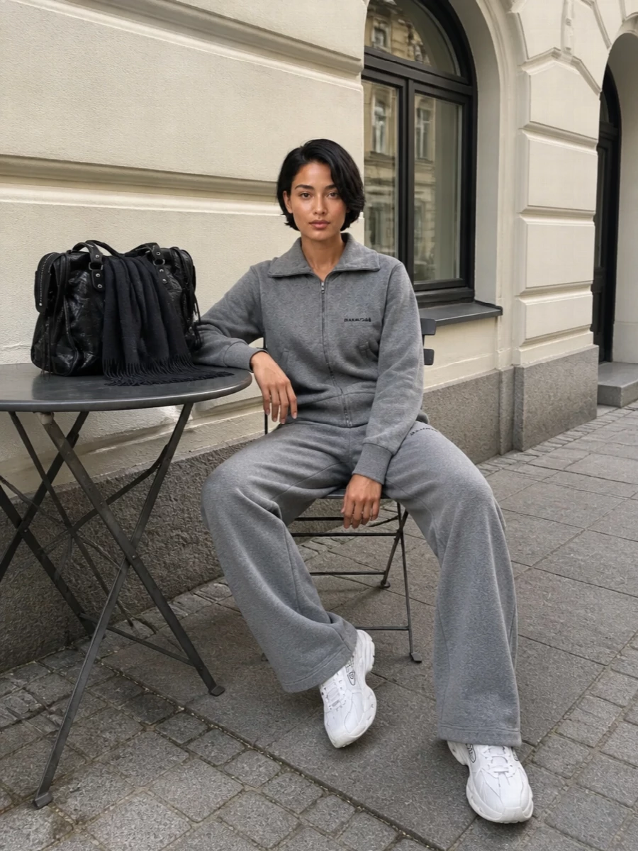 A monochrome grey Balenciaga set keeps everything clean and relaxed, with the wide-leg pant echoing the sweatshirt’s slouch for an easy streetwear uniform. Chunky off white sneakers lighten the base and give it that fashion-runner edge, while a textured black tote and deep charcoal scarf bring just enough structure for city days or long-haul travel. The result is soft, logo-aware and quietly directional without feeling overthought.