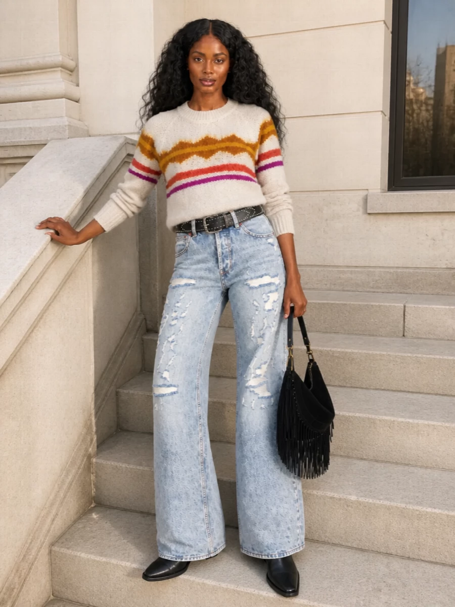 Light-wash distressed flares meet a softly patterned oatmeal knit for a relaxed, boho take on Parisian streetwear. Black western boots, a fringed suede hobo and a studded belt sharpen the attitude and streamline the wide-leg silhouette. The palette stays grounded in warm neutrals with hits of berry and metal so the denim feels intentional rather than casual.