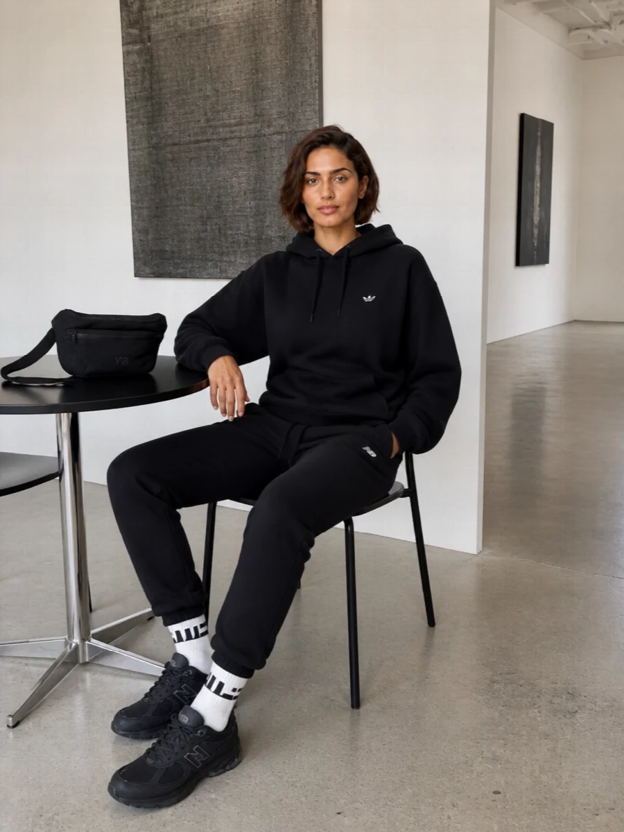 Head-to-toe black keeps this New Balance jogger outfit sharp and unfussy, with the oversized Adidas hoodie echoing its relaxed, sport-first attitude. Stealth New Balance runners and a Y-3 belt bag lean into technical city mileage, while the striped socks add just enough contrast to feel intentional rather than basic. It is an easy off-duty uniform that still reads curated and modern in a monochrome palette.