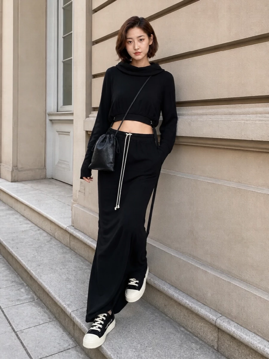 A full Rick-inflected monochrome column: the black jersey maxi skirt anchors the look, paired with the cropped hooded knit to emphasize the waist and elongate the sleeves for that signature slouchy drama. Black DRKSHDW low-top sneakers keep it grounded and street, while the slim drawstring pouch adds just enough hardware and texture without breaking the dark, minimalist line. It’s an easy, nocturnal off-duty uniform that feels deliberate from every angle.