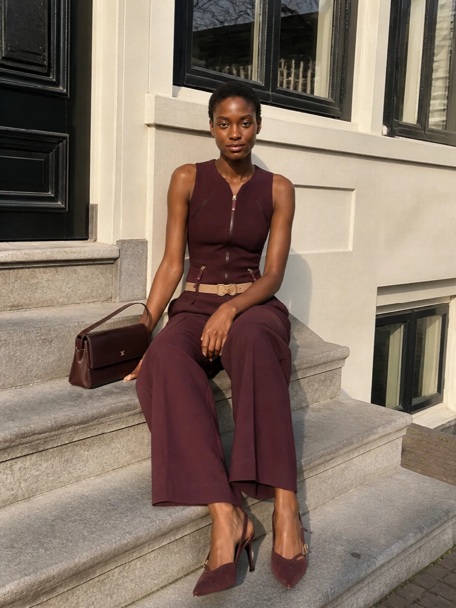 A sculpted burgundy zip-front top meets wide-leg tailored trousers in the same deep tone for a modern, two-piece column that feels sharp yet sensual. Cut-out suede pumps and a linear bordeaux shoulder bag keep the palette tonally rich while the slim belt quietly defines the waist, creating a long, clean line that reads polished for city dinners or formal drinks.