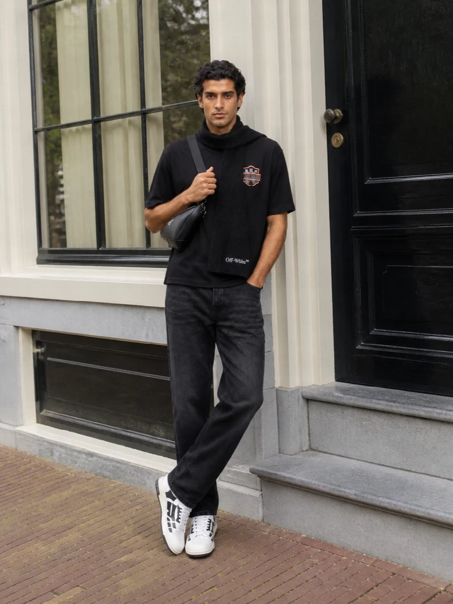 Amiri’s crest tee sits over clean, washed-black straight denim for a street-ready base that feels intentional without going full rock-star. The skeletal-trimmed sneakers bring in bolder graphic energy while staying in the black-and-white story, and the sharp Prada crossbody plus a slim logo scarf keep everything city-functional and polished enough for all-day wear. It reads as modern LA street with just the right amount of logo conversation between each piece.