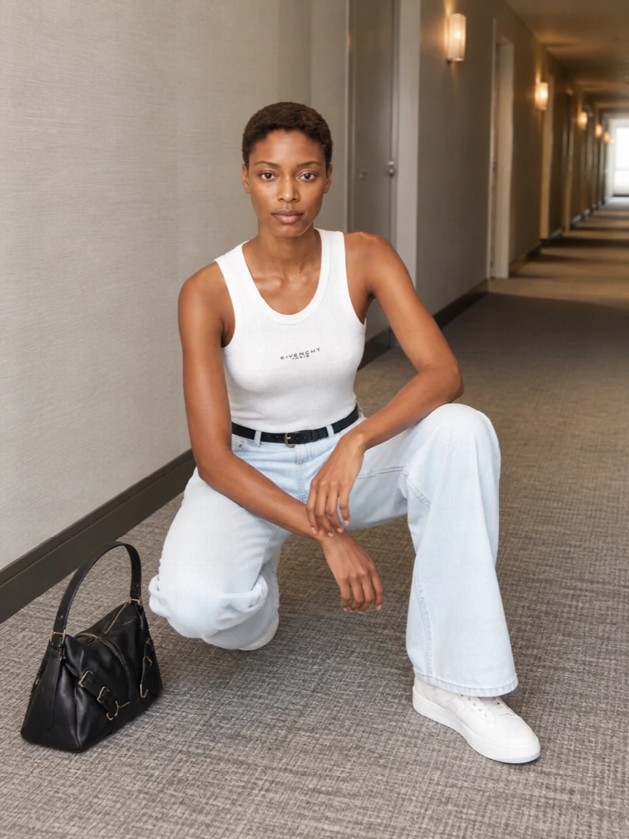 Givenchy’s white ribbed tank sits cleanly against pale wide-leg denim for a lean, modern take on everyday minimalism. White sneakers keep it relaxed and city ready, while a black shoulder bag and slim belt add just enough structure and attitude. The result is a quiet, logo-aware uniform that feels fresh, light and sharply composed for warm days.